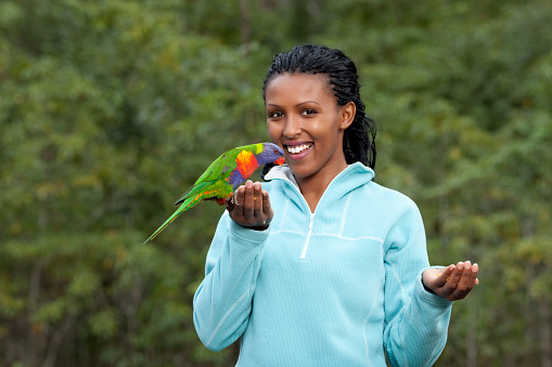 Attractive happy woman with Rainbow Lorikeet parrot in her hand  outdoor in australian rainforest.
