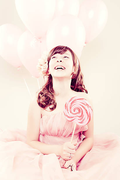 Portrait of a young girl dressed in a pink dress holding a lollipop with a smile on her face.Image is processed from a 16 bit RAW file and profiled in ProPhoto RGB. All my images are professionally retouched.More from this Series: