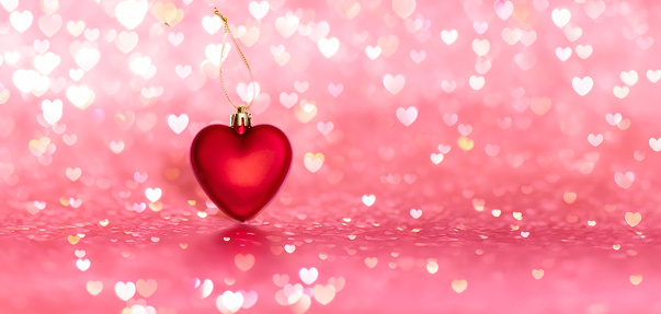 Red glitter heart in front of bokeh pink background. Greeting card for Valentines Day