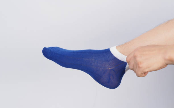 istock Male legs wear blue sock and hand is pulling a sock on white background 1828171977