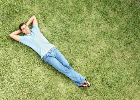 full length of relaxed young man resting in garden with legs crossed at knee