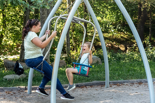 A mother and her son are having fun on a double swing in a sunny forest.