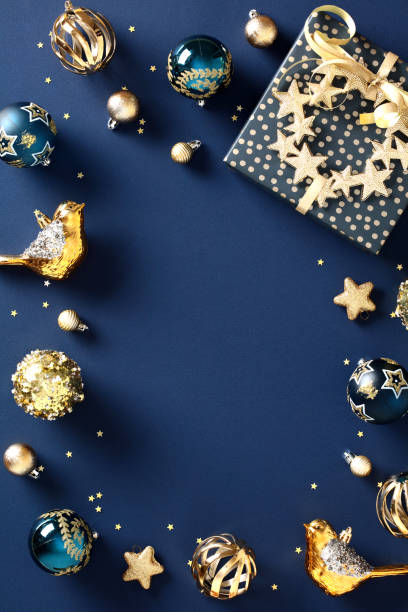 istock Vertical Christmas banner design with gift box, chic decorations, luxury golden balls on dark blue background. Flat lay, top view. 1828195556