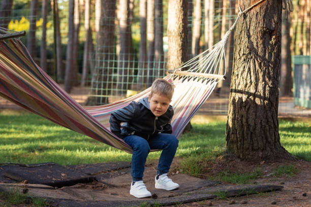 istock Cute little blond caucasian boy having fun with multicolored hammock in the sunny forest. Summer active leisure for kids. 1828196144