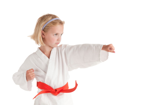 A young blond girl in a gi with an orange belt throws a punch.