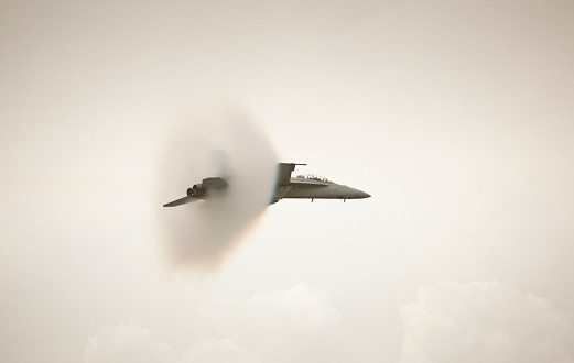 Vapor cone around figher jet about to break the sound barrier (going approx 700mph or 1120km/h). This is the point at which a sudden drop in air pressure occurs, generally accepted as the cause of the visible condensation cloud that often surrounds an aircraft  traveling at transonic speeds. **Slight motion blur and grain.