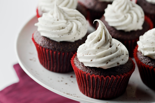 SEVERAL MORE IN THIS SERIES. Red velvet (red chocolate) cupcakes with cream cheese frosting and dusting of cocoa powder on a cake plate.  Shallow DOF.
