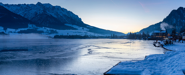 Panorama of the frozen lake Walchsee in Austria during golden hour in a mountain valley on a winter evening.