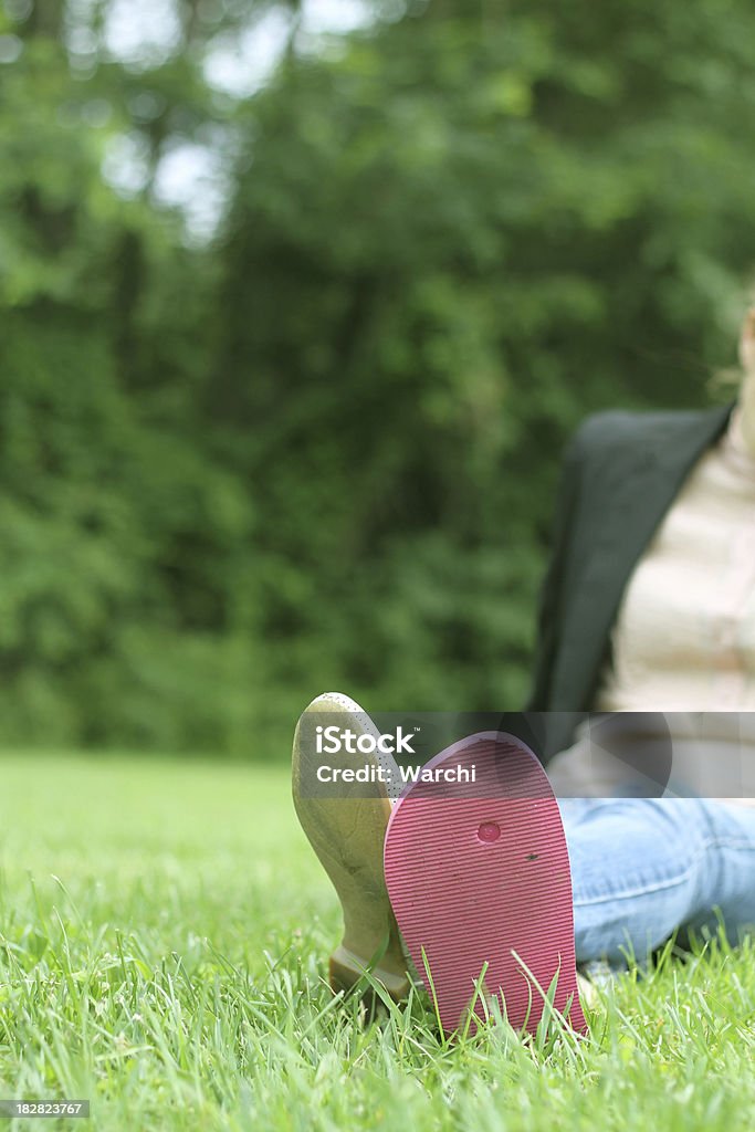 Jovem mulher sentada na grama com dois calçados diferentes - Foto de stock de Ajardinado royalty-free