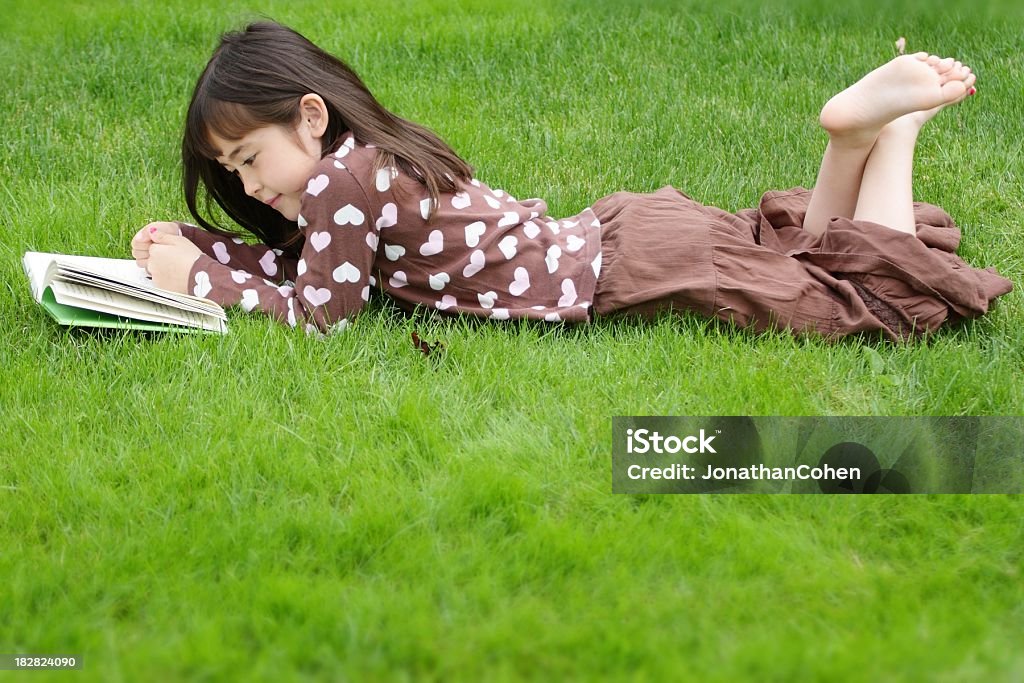 Vista laterale di una bambina leggendo in erba - Foto stock royalty-free di Scalzo