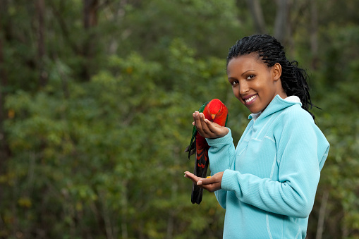 Happy young woman  feeding parrot from both  hands.