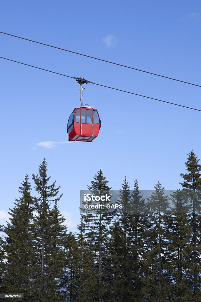 overhead cable car against a blue sky red empty overhead cable car passing the pine trees in the mountains Blue Stock Photo