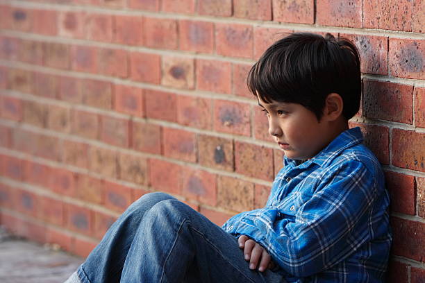 istock Lonely school aged boy slumped against brick wall 182825362