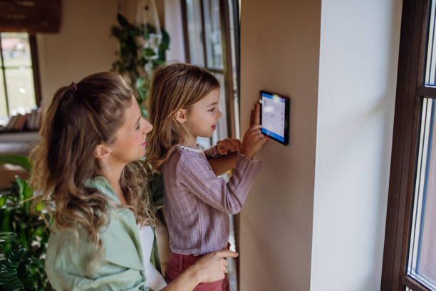 Girl helping mother to adjust, lower heating temperature on thermostat. Concept of sustainable, efficient, and smart technology in home heating and thermostats. stock photo