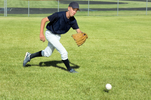 A baseball player chases a ground ball in the outfield.