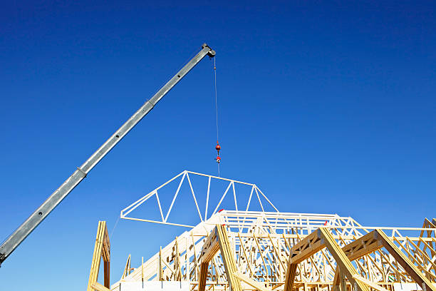 istock Crane Lowering a Roof Truss against Clear Blue Sky 182828071