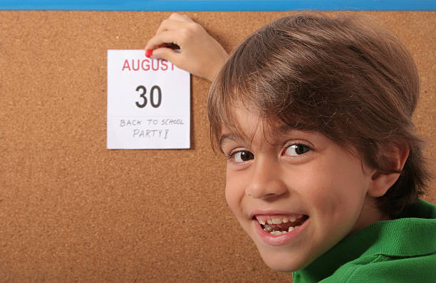 Schoolboy tacking a calendar page onto a cork board to remind a back-to-school party on August 30