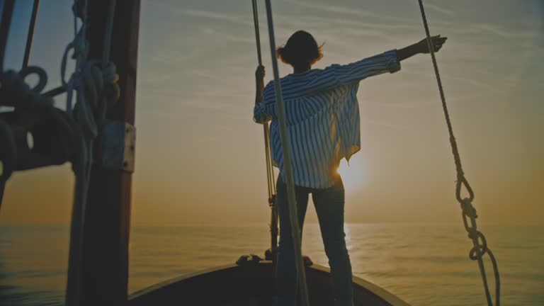 SLO MO Sailing Serenity: A Woman Admiring the Sunset with Arms Outstretched on a Sailboat