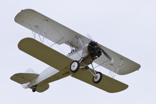 An old white biplane in the air.