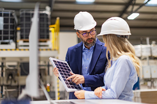 Female engineer and male director talking in modern industrial factory about solar panels installation, solar energy for company. Team management in manufacturing facility. using green renewable energy for business.