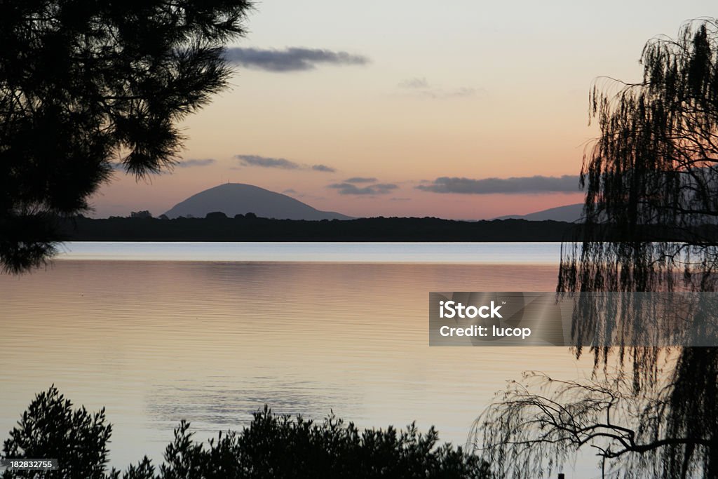 Lagoon at sunset with trees and hill in horizon A DSLR photo of a lagoon landscape at dusk featuring trees silhouettes at the foreground on the border and a beautiful landscape with hills at the horizon line in the background. Water is calm with reflection of the colours of the sky. Located in "Laguna del Sauce" at Punta del Este, Uruguay.  Punta Del Este Stock Photo