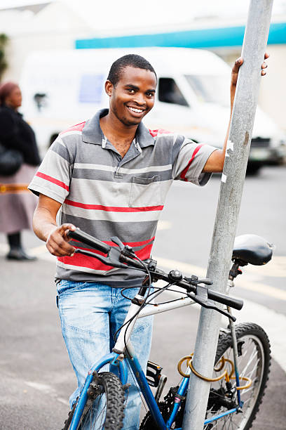 homem africano feliz jovem detém bicicleta, inclinando-se na rua vara - africa african descent south bicycle - fotografias e filmes do acervo