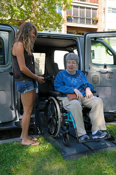 Lowering the Lift A young helper helping a senior citizen exit her handicapped accessible van at curb side. wheelchair lift stock pictures, royalty-free photos & images