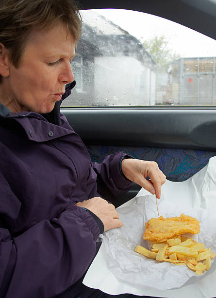 istock Mature woman eating fish and chips in car 182834901