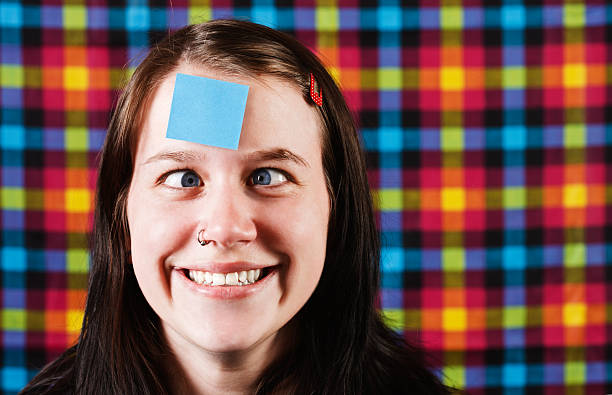istock Zany looking girl squints at blue adhesive note on forehead 182835725