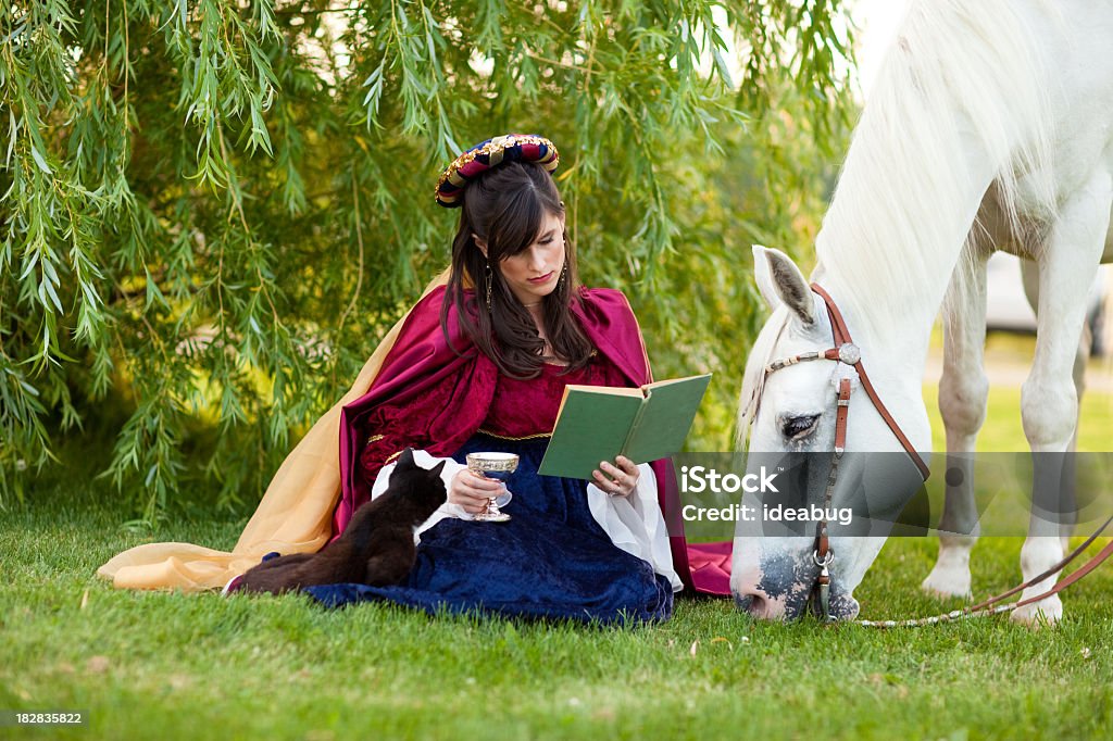 Mujer joven usando Renaissance vestido lectura por debajo de árbol con caballos - Foto de stock de Renacimiento libre de derechos