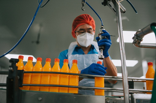 Asian Chinese male juice factory worker sealing bottle cap of orange juice in production line