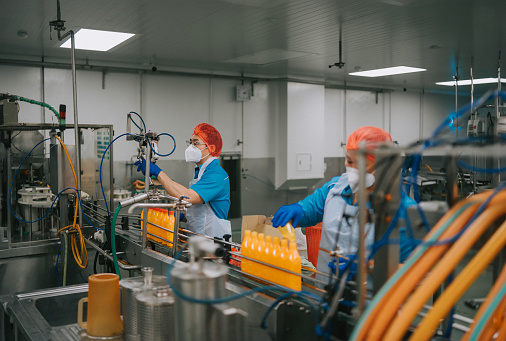 Asian Chinese juice factory worker sealing bottle cap of orange juice in production line