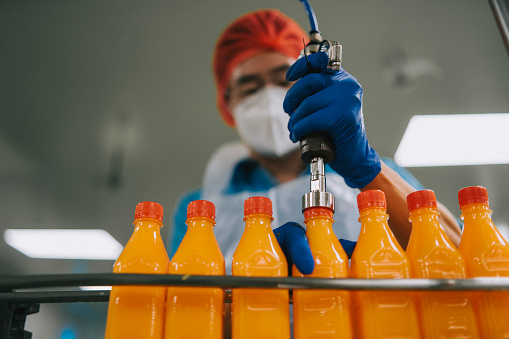 Asian Chinese male juice factory worker sealing bottle cap of orange juice in production line