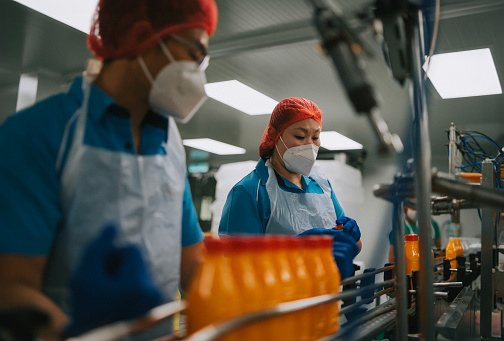 Asian Chinese juice factory worker sealing bottle cap of orange juice in production line