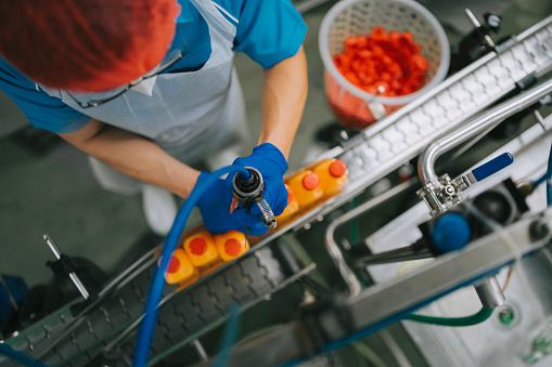 high angle view Asian Chinese juice factory worker sealing bottle cap of orange juice in production line
