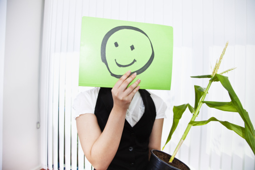 image of some emoticons cut out of orange paper with a sad face surrounding a big green emoticon with a smiling face. concept of bad influences, bad friendships, negativity, problems, bullying...