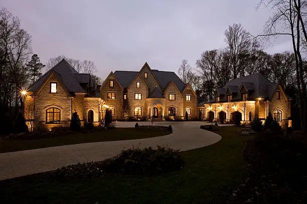 Long winding driveway leading up to the main entrance of elegant stone mansion in the evening. Horizontal shot.