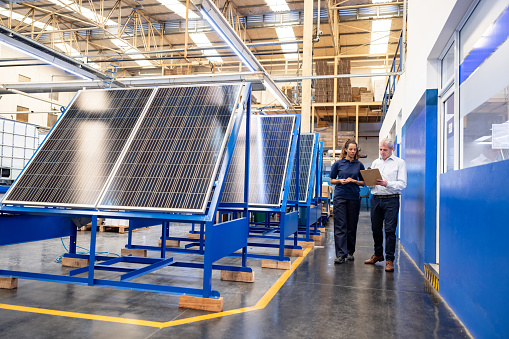 Foreperson talking to a worker while supervising the operation of solar panels at a factory