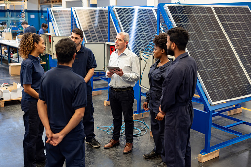 Latin American foreman talking to a group of employees in a staff meeting at a green factory next to solar panels