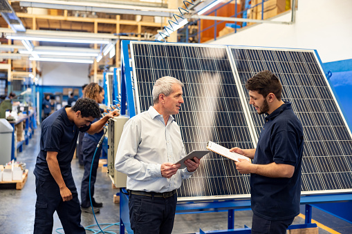 Latin American foreperson talking to an employee about the use of solar power in a manufacturing factory - green technology concepts