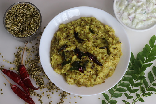 Wholesome Moong Dal Kichadi paired with refreshing cucumber raita, a balanced Indian meal. Shot on white background along with a bowl of moong dal