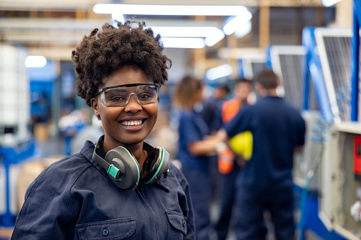 Happy African American female employee working at a solar panel factory wearing protective workwear and looking at the camera smiling