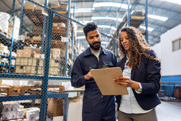 gerente conversando com um funcionário em um armazém industrial - inspector clipboard businesswoman white collar worker - fotografias e filmes do acervo