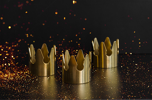 Epiphany  Day or Dia de Reyes Magos concept. Three gold crowns on black background with golden particles.