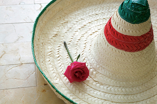 A closely cropped woven mexican sombrero with a rose on it sitting on a tile floor.