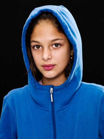 Ten years old hispanic little girl posing looking at the camera wearing a hoodie on black background (this picture has been shot with a super high definition Hasselblad HD3 II 31 megapixels camera)