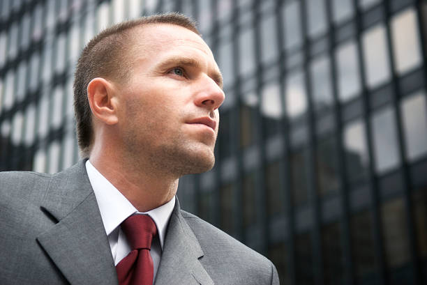 Businessman Looks Serious Skyscraper Background Businessman looks serious against the dark glass and steel of an office building crew cut stock pictures, royalty-free photos & images