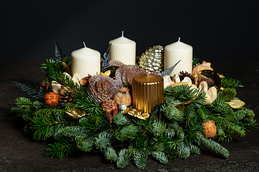 Decorative wreath of four white and gold Advent candles in an Advent wreath decoration on a dark background on spruce branches. Tradition before Christmas. Festive still life.