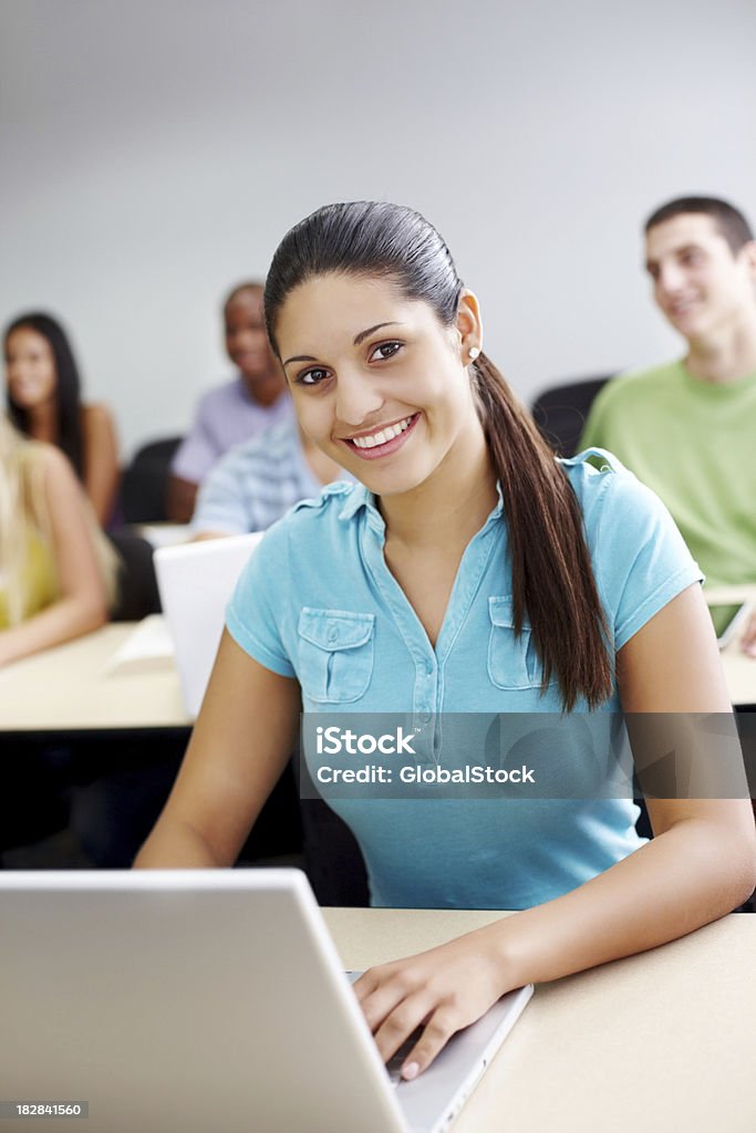 Donna sorridente utilizzando un computer portatile con gli amici in background - Foto stock royalty-free di 20-24 anni