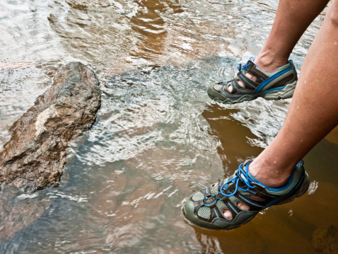 Close up of someone wearing water shoes sitting with legs hanging over the river.